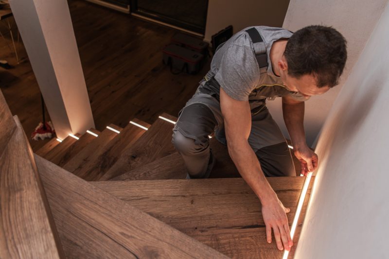 Man installing LED lighting strips along stair treads